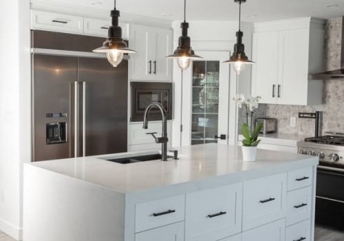 Black pendent lights over quartz counter top with over size stainless fridge in this newly renovated kitchen.