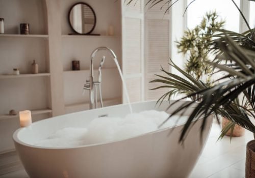 Soft native hues organic shapes look of bathroom with big window oval bathtub in neutrals tones. Green palm plants candles bubblebath leasure and relaxation skin selfcare wellness luxury living